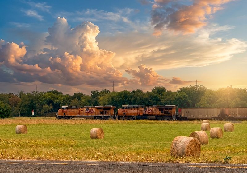 Freight train crossing the farmland past round hay bales at golden hour near The Waxahachie Tiny Home