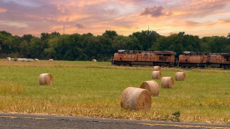 Round hay bales in the field behind The Waxahachie Tiny Home with a freight train at sunset